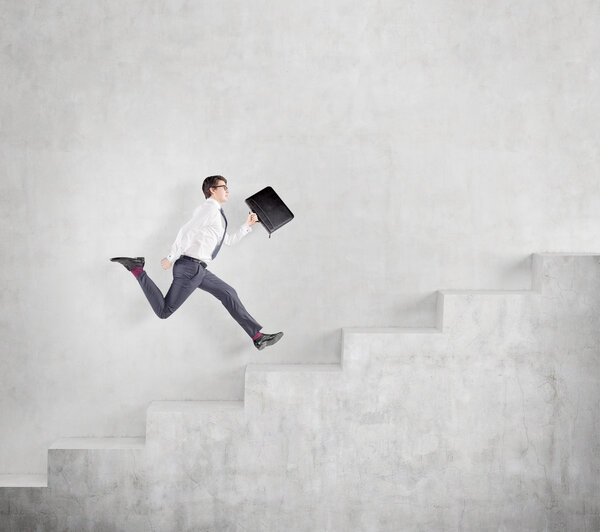 Young businessman with a folder running fast up a a concrete stairs along a concrete wall.