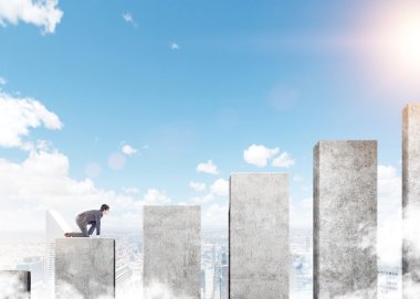 A young businessman ready to climb a career ladder in shape of a concrete bar chart, blue sky at the background. Concept of career growth.