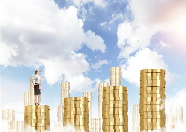 A young businesswoman looking in front ready to climb a career ladder in shape of a bar chart made of coins, blue sky at the background. — Stockfoto