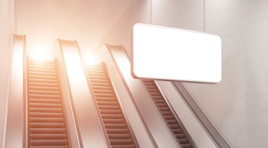 An escalator in the underground. A blank horizontal poster hanging in front of it.