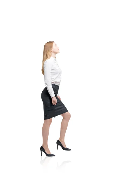 A young woman with loose red hair in a blouse and skirt, high heels in the posture of making a step up. — Stockfoto