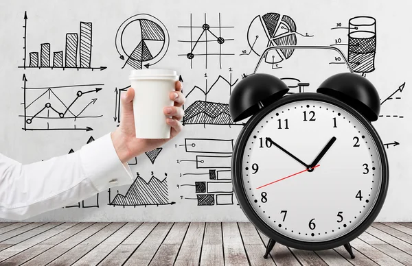 hand holding a paper cup, the word 'pause' written over it. Black alarm clock to the right. White background. Concept of coffee break.
