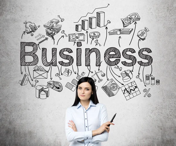 Uma jovem mulher bonita de pé com as mãos cruzadas e segurando uma caneta, a palavra 'negócio' e numerosos símbolos de negócios sobre sua cabeça . — Fotografia de Stock