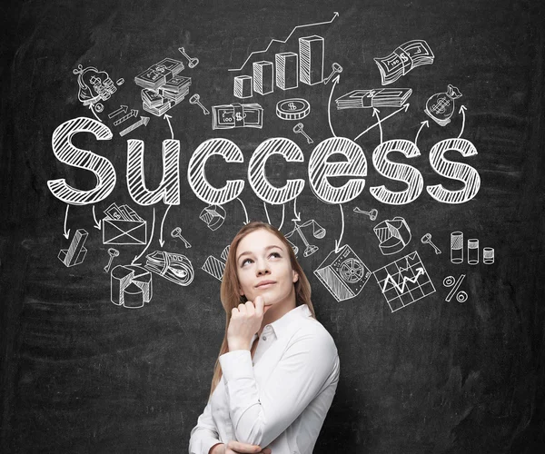 A young woman with hand to the chin looking up and standing in front of a blackboard with many different business icons and the word 'success' drawn on it. — ストック写真