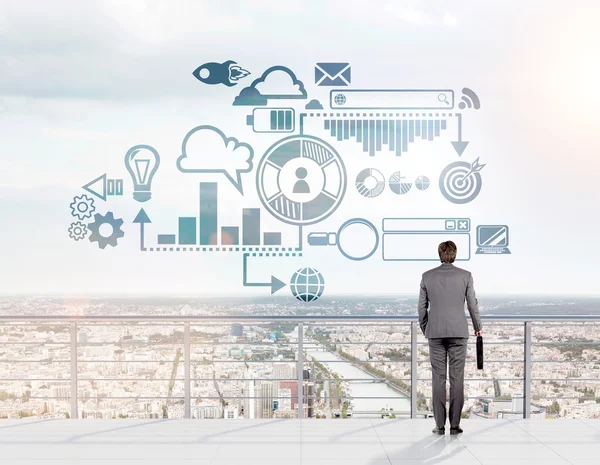 A businessman with a case in hand standing on a roof looking at a city panoram, a business scheme in front of him. — Stock Photo, Image