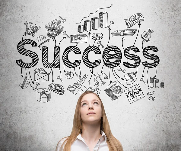 A young woman looking up and standing in front of a conrete wall with many different business icons and the word 'success' drawn on it. — Stok fotoğraf