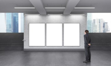 A man looking at three blank vertical billboards in the subway crossing, stairs up on both sides, Singapore seen from it.