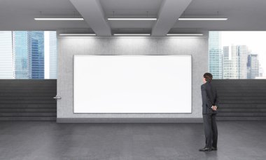 A man looking at a big blank horizontal billboard in the subway crossing, stairs up on both sides, Singapore seen from it.