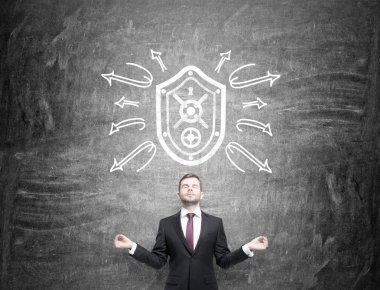 A man in the posture of meditation with eyes closed standing under a shield drawn on the blackboard, arrows around the shield as if rebounding from it.