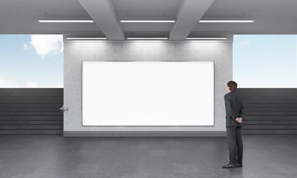 Un hombre mirando una gran cartelera horizontal en blanco en el cruce del metro, escaleras a ambos lados, cielo azul visto desde ella . — Foto de Stock