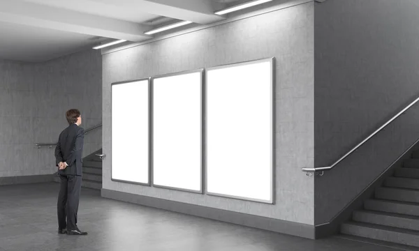 A man standing in front of three blank vertical billboards in the underground, stairs up on both sides. — Φωτογραφία Αρχείου