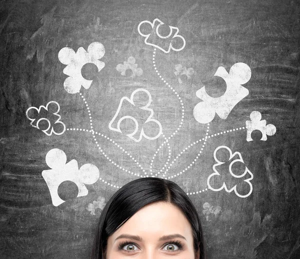 A beautiful young woman  at a blackboard with parts of a puzzle drawn on it, looking in front. — Stock Fotó