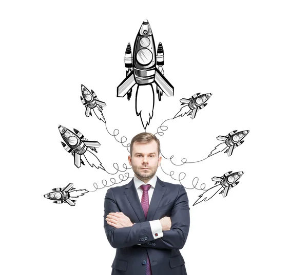 A serious young man with hands crossed standing at a white wall and looking in front of him, painted rockets flying from over his head. — Stock Photo, Image