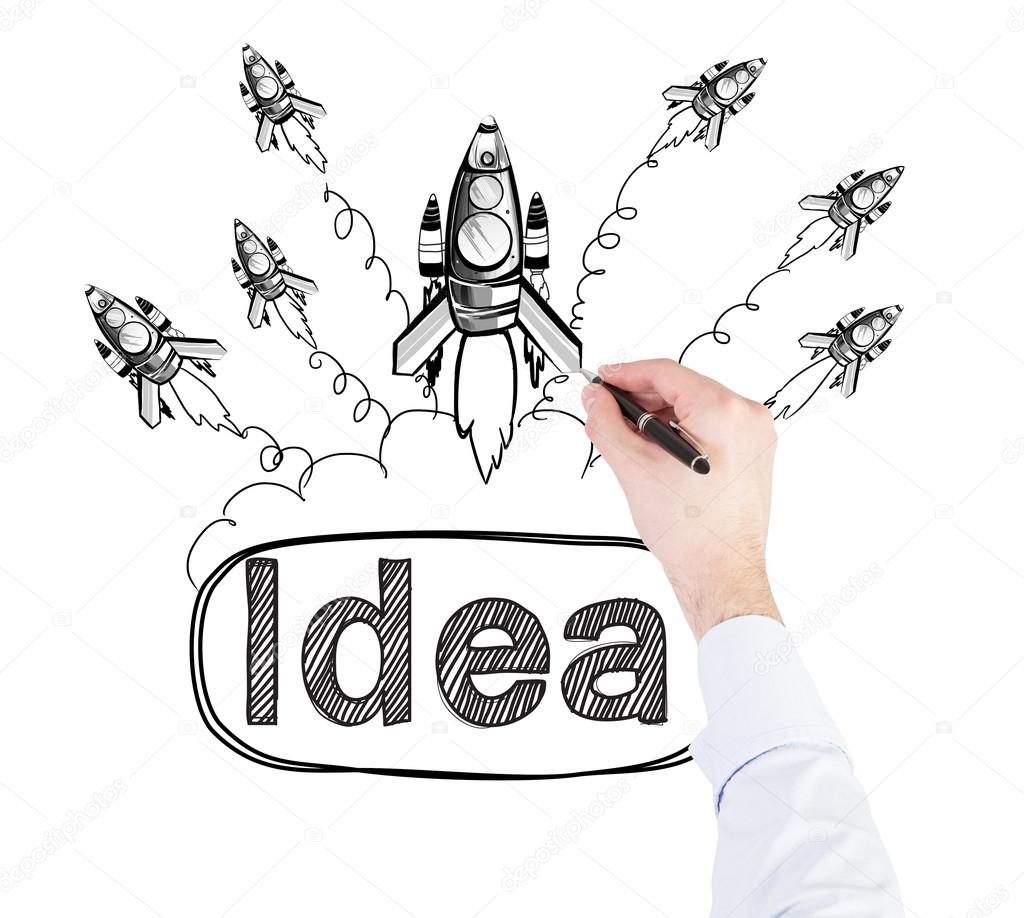 A hand drawing rockets on a white wall, the word 'idea' written under them.