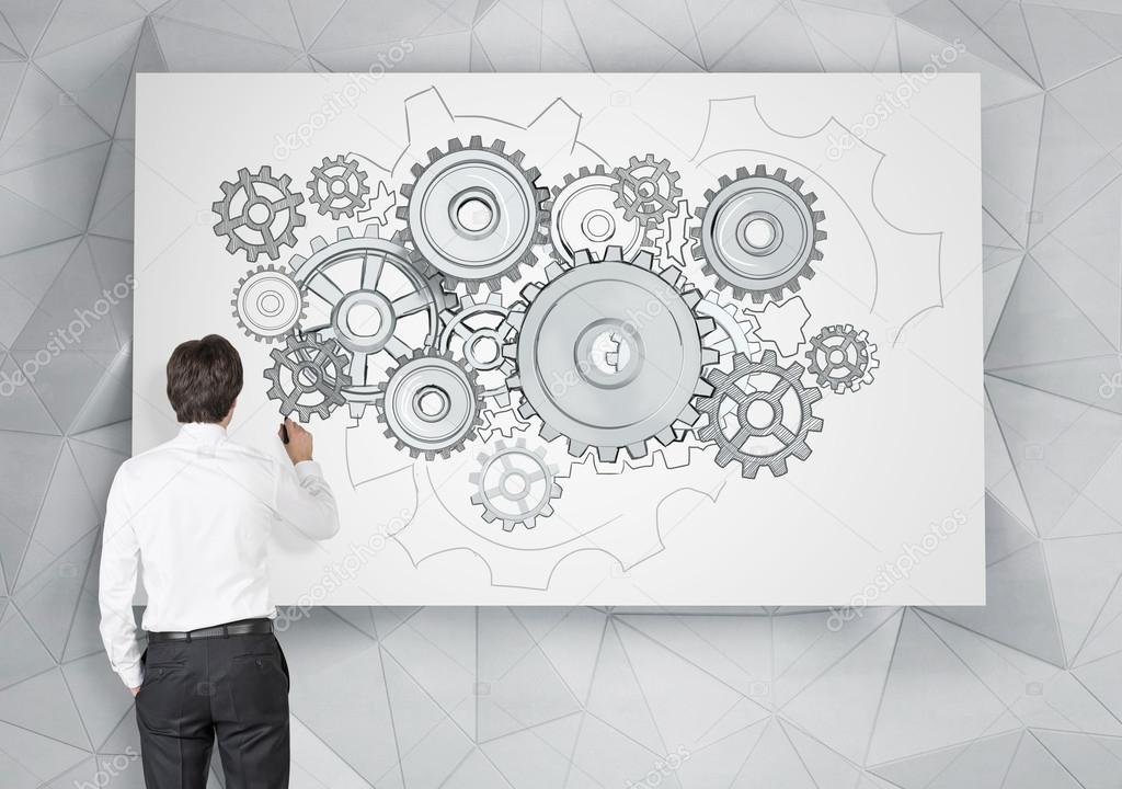 A man drawing cogwheels on a white poster with a pen.