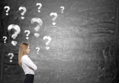 A young businesswoman with hands crossed thinking about a problem, many question marks painted over her.