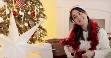 Neşeli kadın gülümsüyor ve dans ediyor Noel ağacının yanında oturuyor, neşeli bir ruh hali içinde..