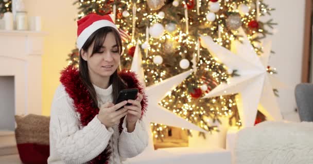 Mujer feliz en sombrero rojo de Navidad está llamando en el teléfono inteligente y sonriendo. — Vídeo de stock