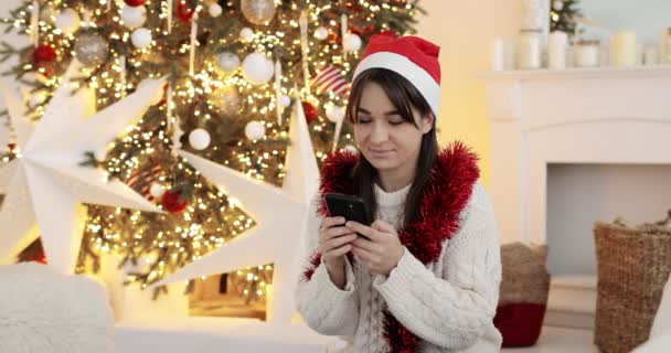 Joyeux jeune femme en chapeau de Noël rouge parle sur smartphone et souriant. — Video