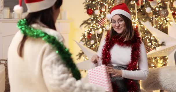 Две подруги молодые женщины празднуют Рождество вместе и дарят подарки друг другу. — стоковое видео