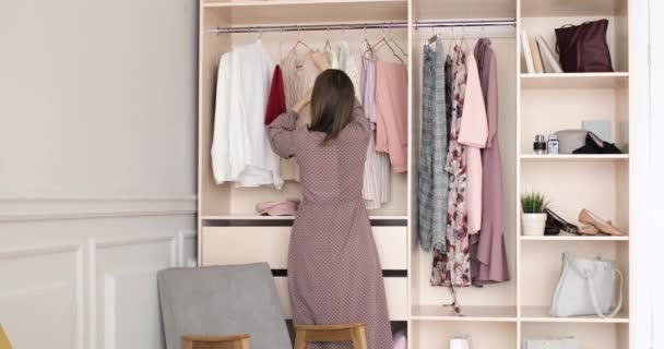 Vrouw in jurk is het kiezen van kleding op een rek in de kast op zoek naar wat te dragen. — Stockvideo