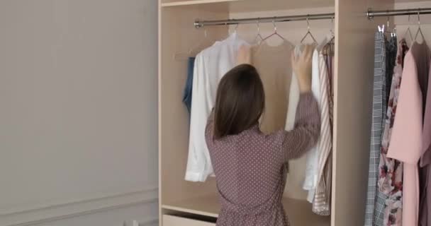 Frau sucht Kleider im Kleiderschrank zu Hause aus und probiert zwei Pullover aus. — Stockvideo