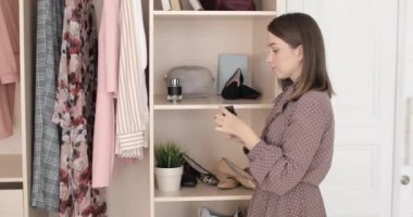 Zarif genç bir kadın, evdeki gardırobun yanında vücuduna parfüm sıkıyor..