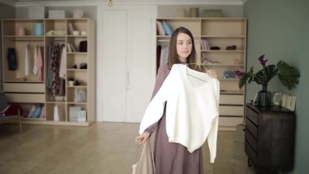 ドレスの若い女性はしようとしている2つのセーター前ミラーでワードローブルーム. — ストック動画