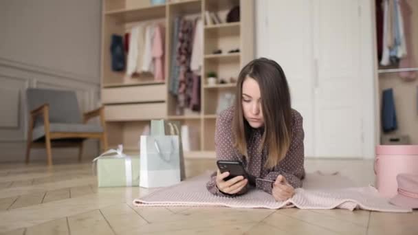若い女性は自宅で敷設スマートフォンやクレジットカードを使用してオンラインで支払いをしています. — ストック動画
