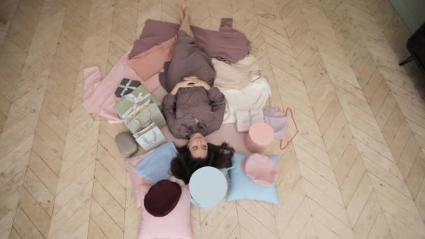 Top view of woman is lying on floor surrounded by boxes, bags and clothes. — Stock Video