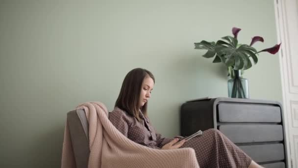 Elegant ung kvinna läser tidningen sitter i fåtölj hemma, sidovy. — Stockvideo