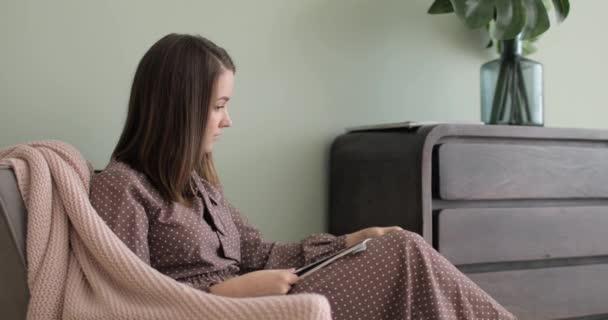Portret młoda kobieta czyta magazyn siedzi w fotelu w domu, widok z boku. — Wideo stockowe