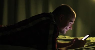 Adam akıllı telefonlara bakıyor sosyal medyada sohbet ediyor yatakta yatıyor, yandan bakıyor.