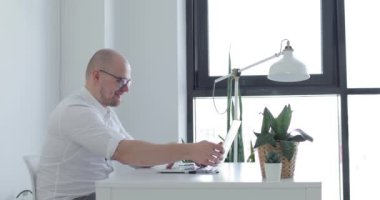 Genç adam dizüstü bilgisayarın önünde oturup sohbet ediyor. Yan görünüm.