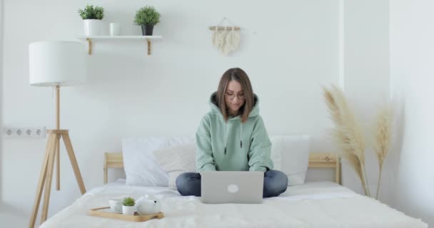 Молодая красивая женщина сидит на кровати перед ноутбуком и работает. Вид спереди. — стоковое видео