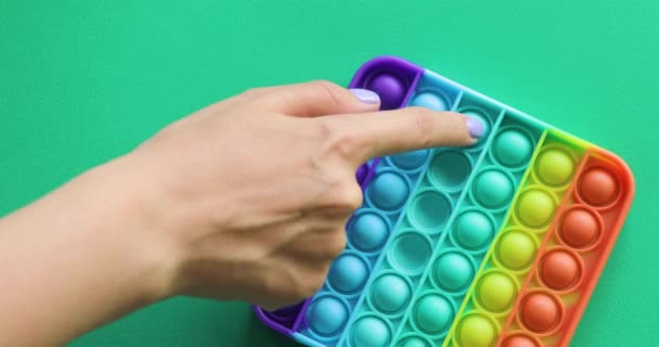 Handen spelen met antistress pop het speelgoed. Regenboog zintuiglijke fidget geïsoleerd op groene achtergrond. — Stockvideo