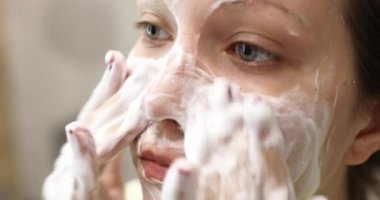 Genç bir kadın yüzüne köpük temizleyici sürüyor. Günlük yüz bakımı prosedürü.