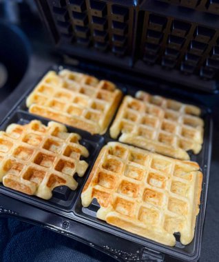 Waffle makinesinin içinde duran taze pişmiş altın waffle. Sıcak renkler ve taze dokular ev yapımı lezzetli bir kahvaltıyı ön plana çıkarıyor..