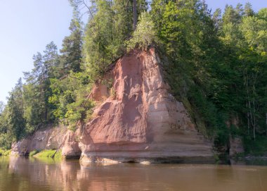 Nehirde güzel bir gün, kumtaşı kayalıkları ve sudaki ağaç yansımaları, mavi gökyüzü nehir suyuna yansıyor, Gauja nehri, Letonya