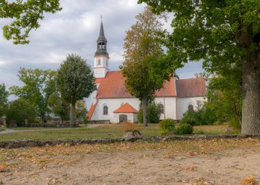 Kırmızı çatılı beyaz kilise, sonbahar renklerinde ağaçlarla çevrili kilise çanı kulesi, Burtnieki Kilisesi, Letonya