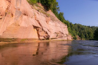 Nehirde güzel bir gün, kumtaşı kayalıkları ve sudaki ağaç yansımaları, mavi gökyüzü nehir suyuna yansıyor, Gauja nehri, Letonya