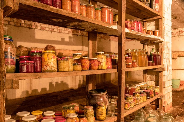 Evin bodrumunda konserve kavanozlu fotoğraf, tahta raflarda farklı şekillerde kavanozlar, çeşitli konserve yiyecekler, sonbahar hasat zamanı, kış için stoklar.