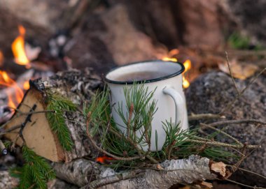 Sonbahar zamanı şöminenin yanında çay ısıtan metal bardaklar, yanan odun, dallar ve duman, sonbahar zamanı