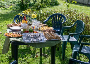 Bahçe partisi için bir sehpa, masada çeşitli tabaklar, çimen plastik masa ve sandalyeler.