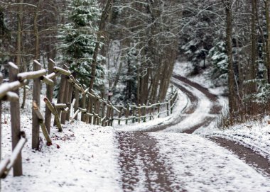 Karlı yollu kış manzarası, karla kaplı ahşap çitler, yol kenarındaki ağaçlar ve çalılar, kış günü