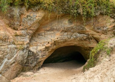 Kum taşı duvar ve mağaranın girişi, mağara Priedaine Mağarası, Cesu Bölgesi, Letonya 'da küçük bir nehrin kıyısında yer almaktadır.