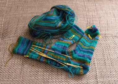 Yeşil çizgili iplikle örülmüş çorap, ahşap örgü iğneleri, yün yumağı, hobi olarak el işi, örgü konsepti, el işi.