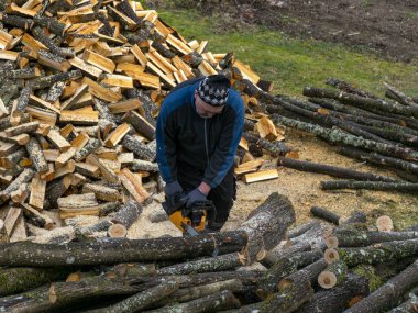Ön planda odun, odun ve kütük kesen bir adamın resmi.
