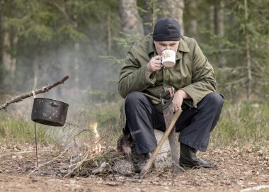 Ormandaki bir orman korucusu dinlenirken çay içer, ormandaki bulanık arka plan, üzerinde bir demlik olan şenlik ateşi, sonbahar ormanında.