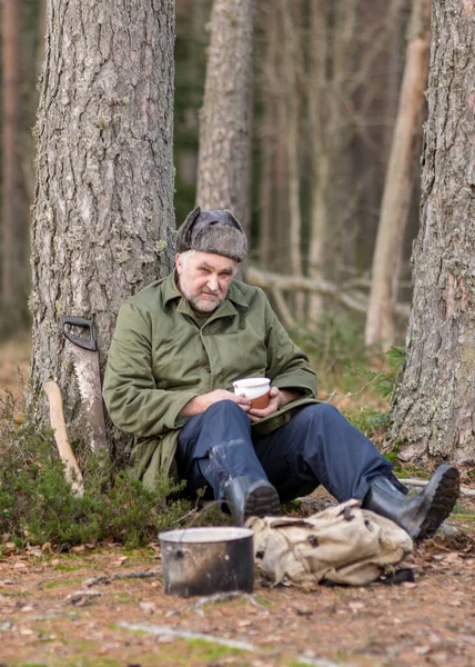 a forester in the forest drinks tea at rest, blurred forest background, bonfire with a pot over it, in the autumn forest